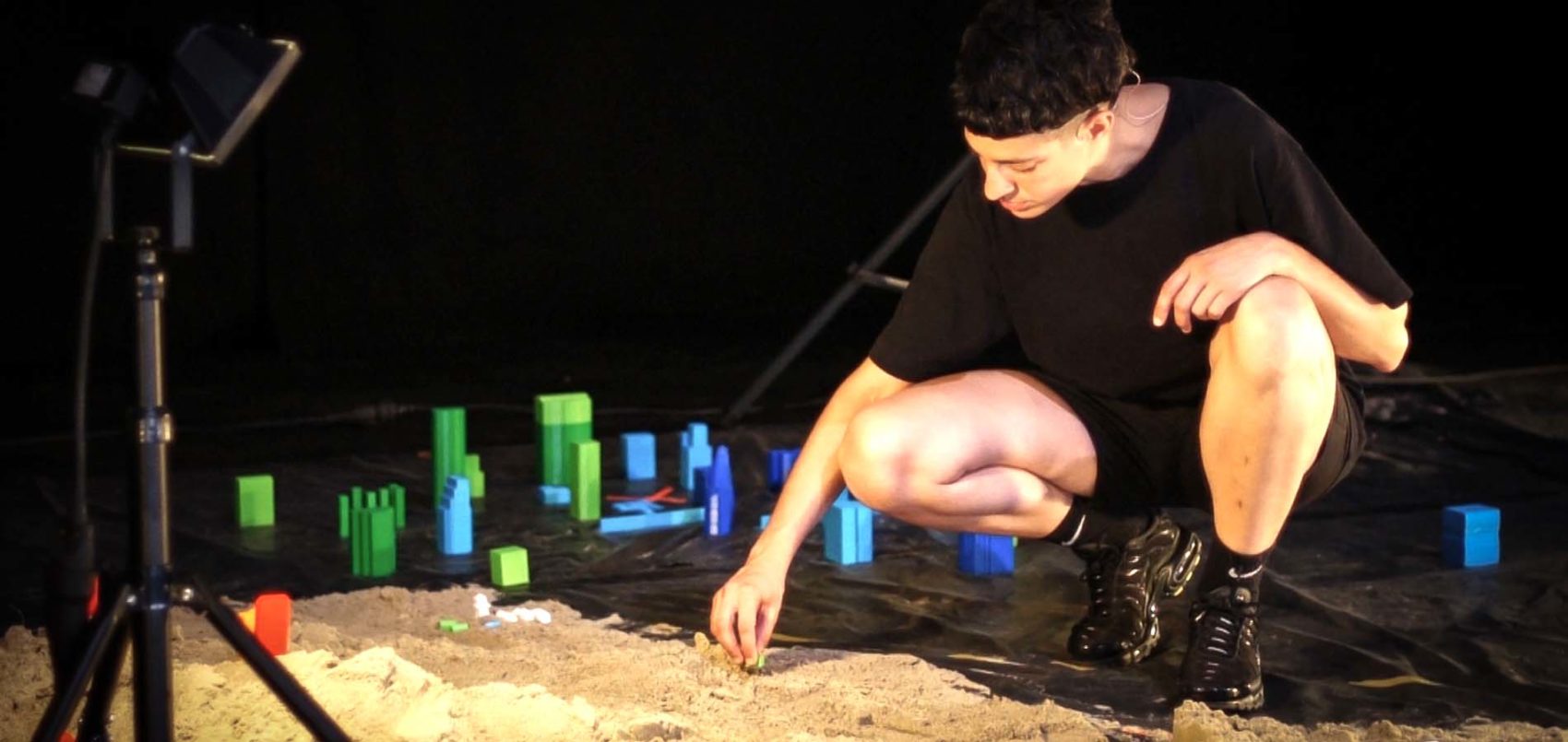 Léa Drouet sur scène, accroupit devant du sable et des immeubles miniatures