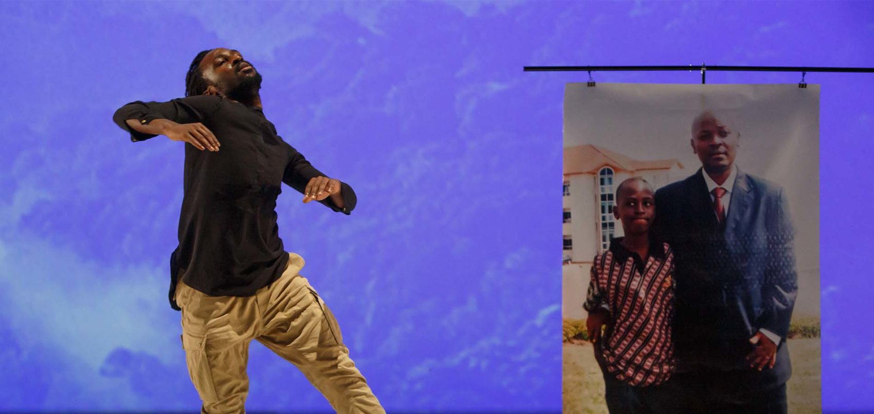 Sur scène un homme danse avec un poster de la photo d'une homme et son fils, à sa gauche