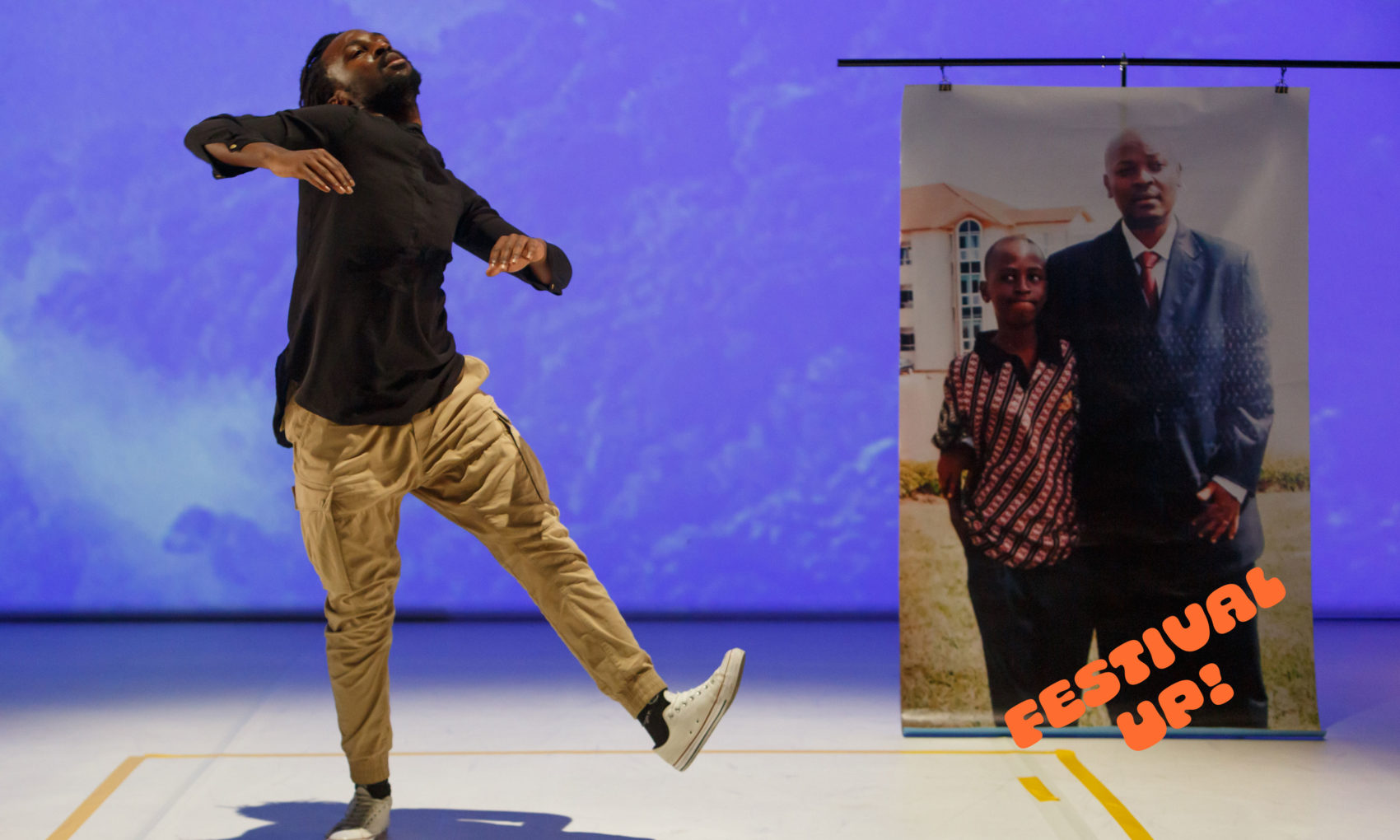 Sur scène un homme danse avec un poster de la photo d'une homme et son fils, à sa gauche