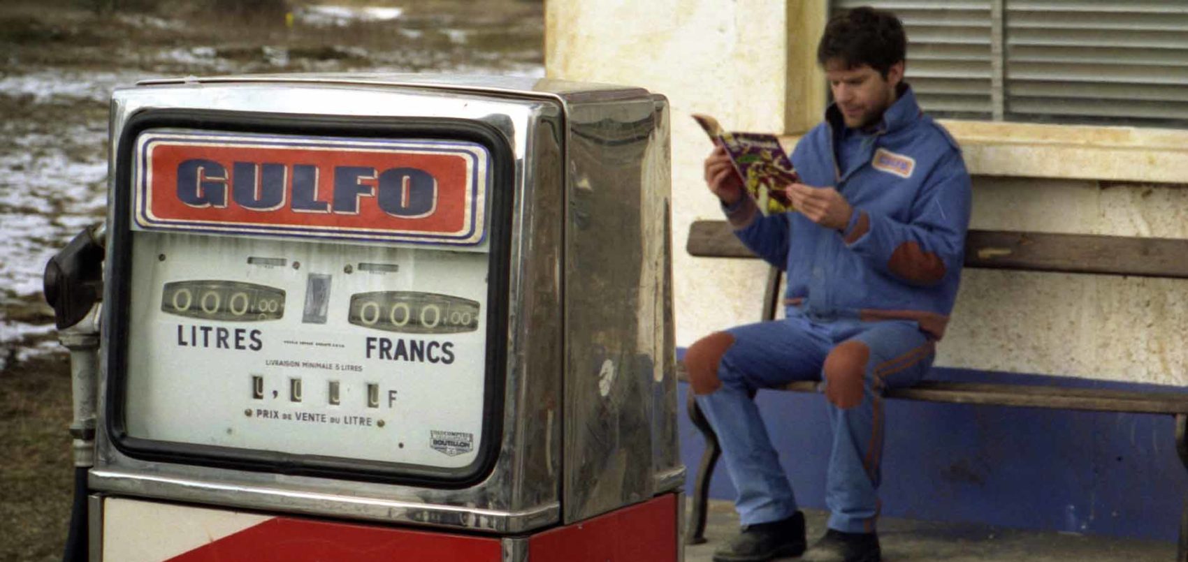 Un homme en train de lire un revue devants une station service 