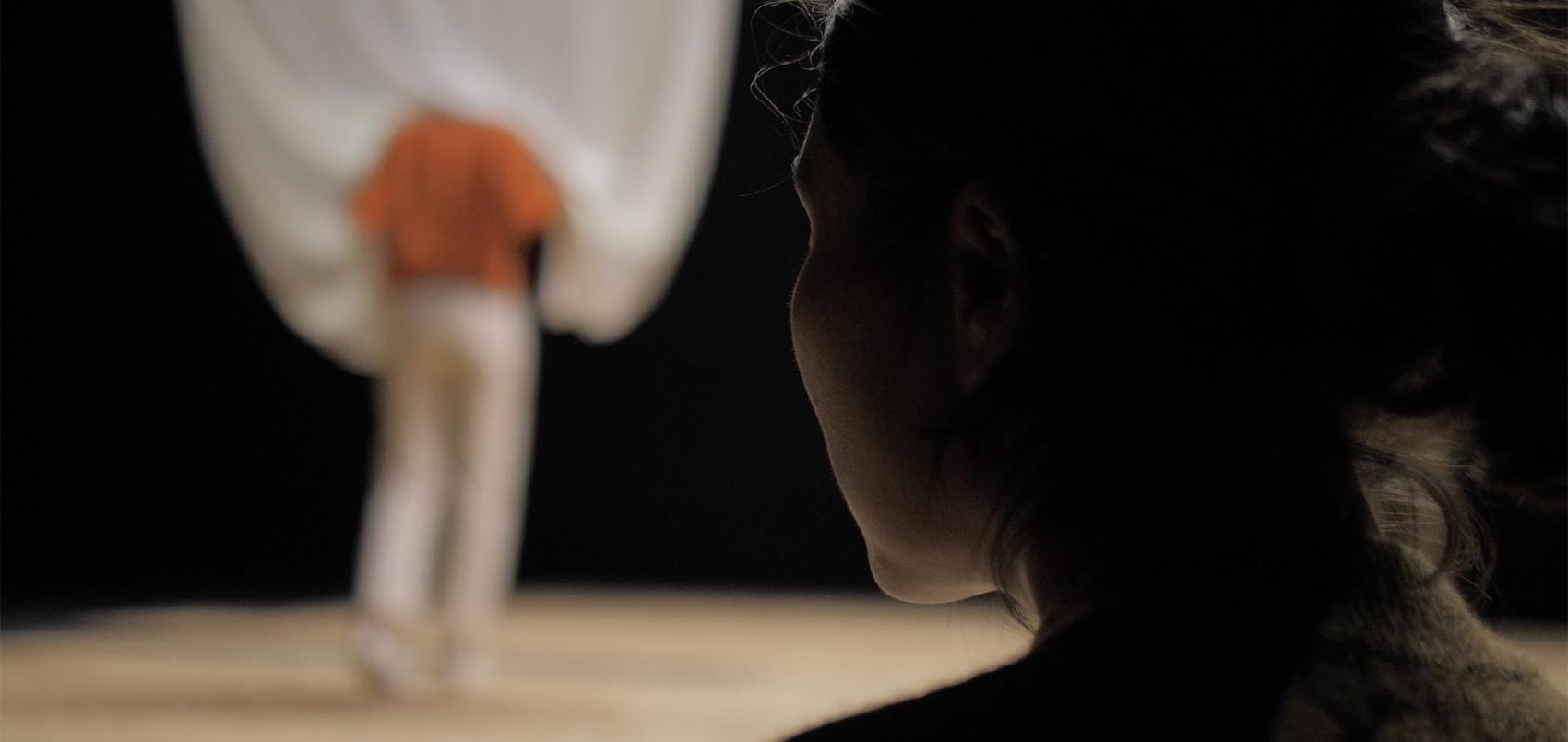 Une femme de dos avec en fond une silhouette flou tenant un drap blanc