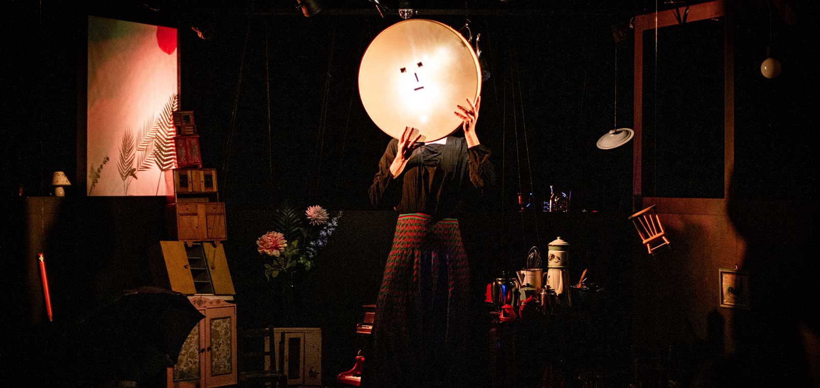 Alice Dourlen est debout au milieu de la scène avec un objet rond avec des yeux, un nez et une bouche. Elle est entourée de petits objets
