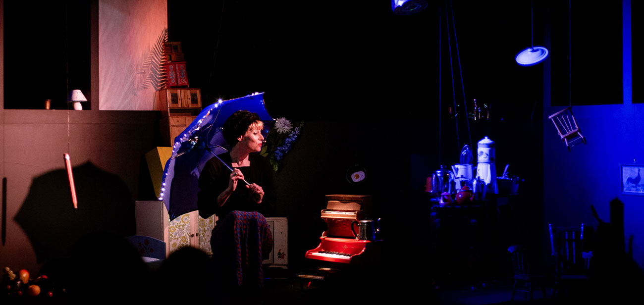 Alice Dourlen est assise avec un parapluie sur l'épaule et est entourée de petits objets