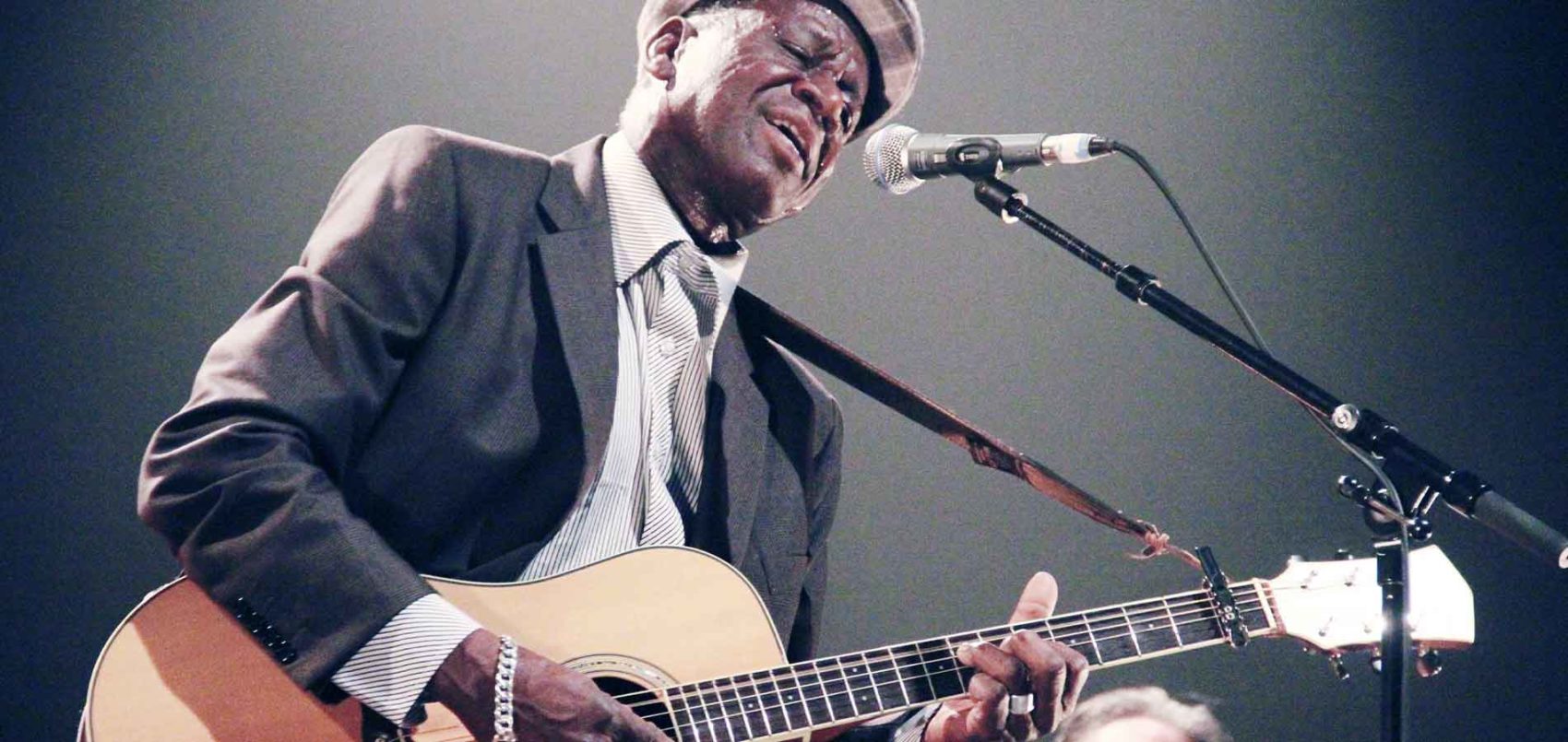Boubacar Traoré chante dans un micro et fait de la guitare