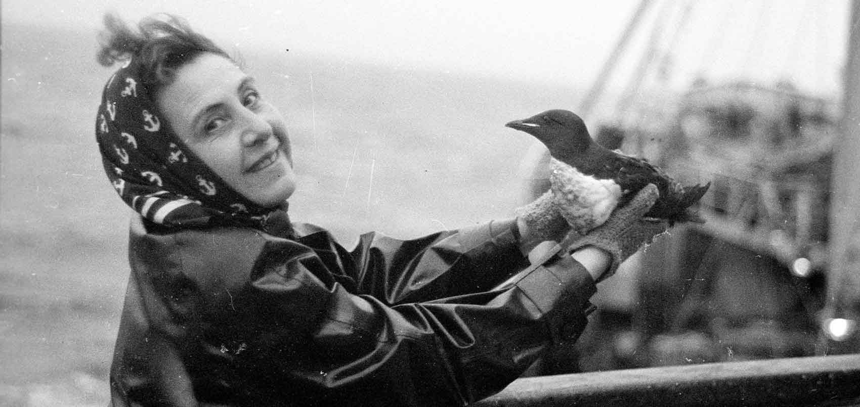 Une femme, sur un bateau, regarde la caméra en tenant un oiseau dans ses mains