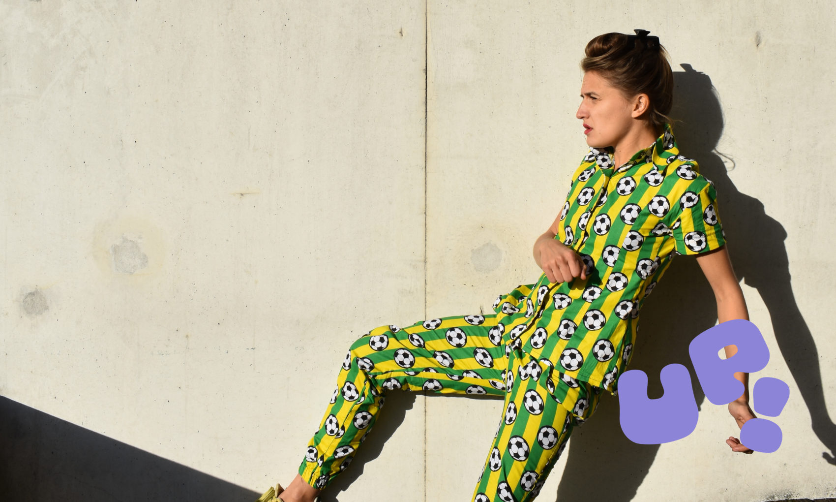 Une femme est en mouvement, de profil et porte un ensemble vert et jaune avec des ballons de foot