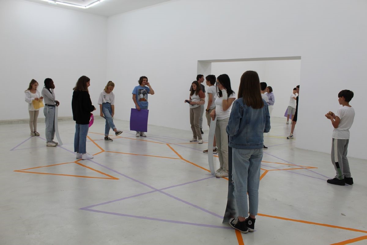 Dans une salle blanche, des collégiens sont placés sur des lignes de couleurs tracées au sol