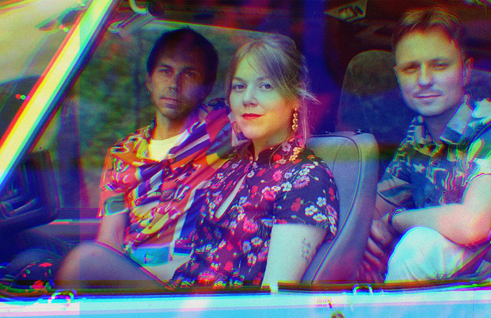 Photo du groupe Simone d'Opale dans une voiture, avec une femme au centre et deux hommes autour. Ils portent des chemisettes à fleurs