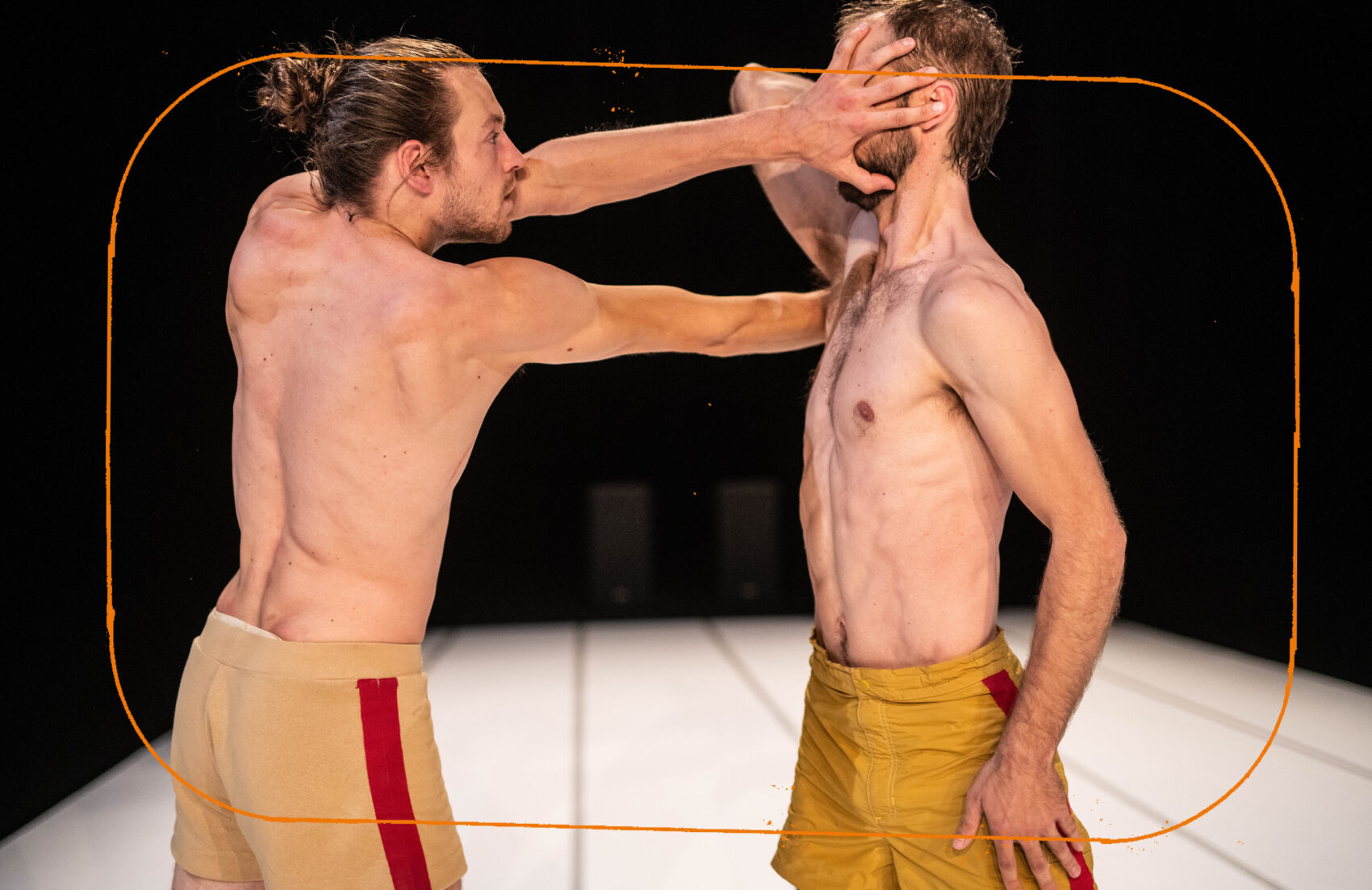 Deux hommes torse nu face à face qui se touchent le visage avec leurs bras