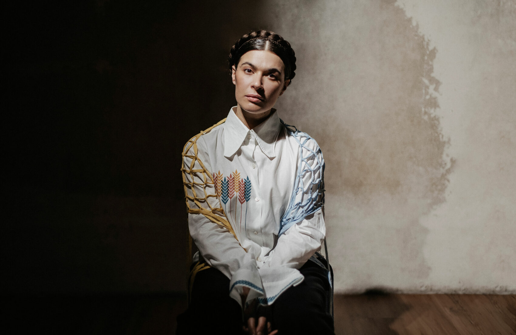 Portrait de Ganna, assise sur une chaise de face. Avec une tresse dans les cheveux et une chemise blanche avec des broderies