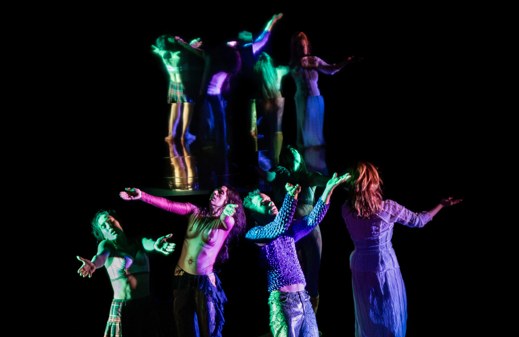 Quatre danseurs et danseuses avec les  bras en l'air et des costumes fluo
