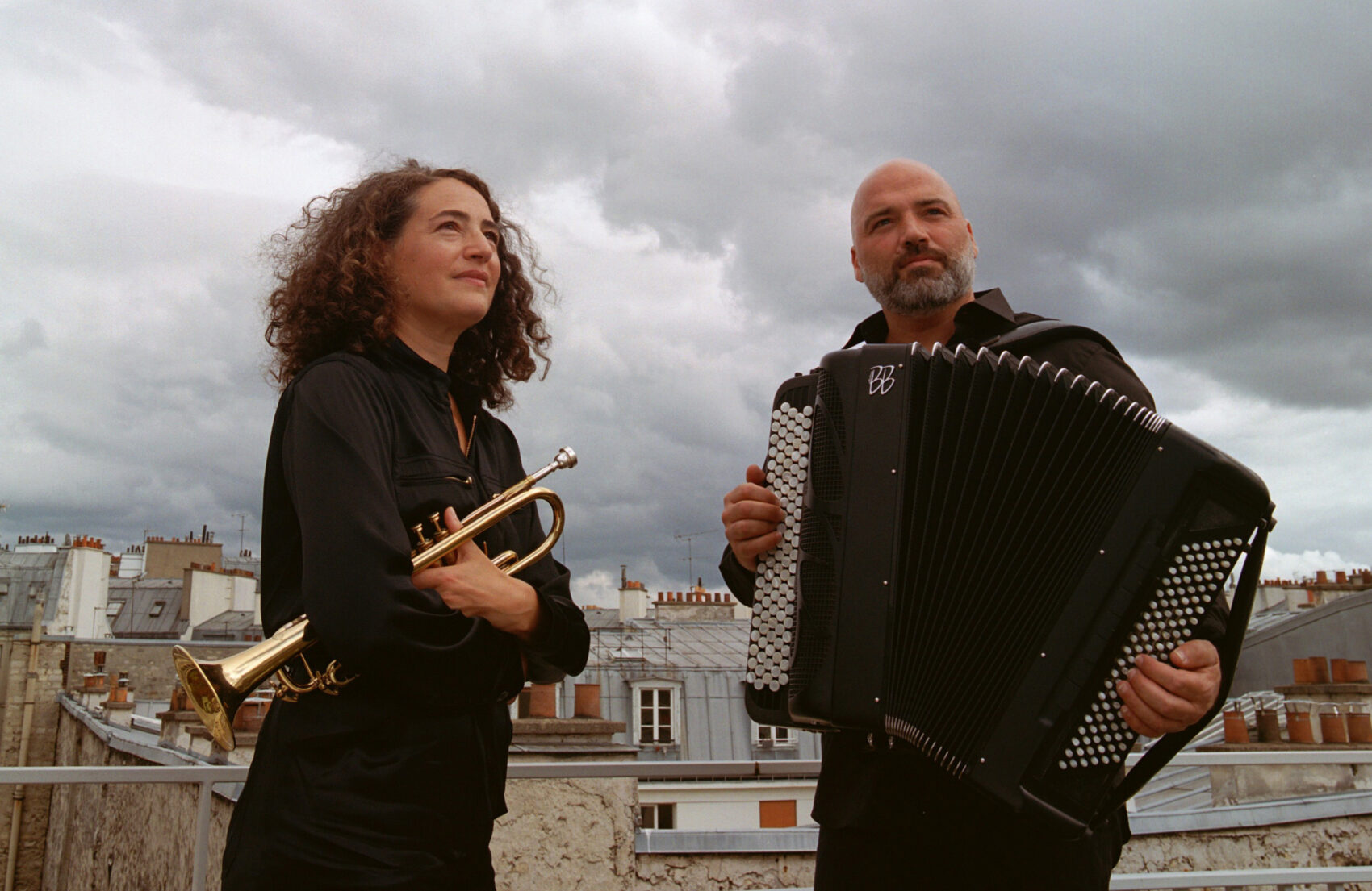 Photo du duo avec à gauche Airelle Besson avec sa trompette et à droite Lionel Suarez avec son accordéon. Ils sont devant des toits 