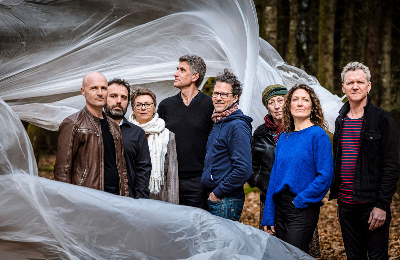 Photo avec 5 musiciens et 3 musiciennes du groupe avec une bâche blanche qui vole